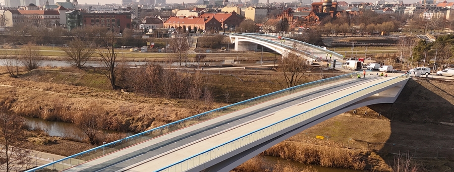 Na zdjęciu widać dwie kładki pieszo-rowerowe z lotu ptaka. W oddali widać zabudowania.