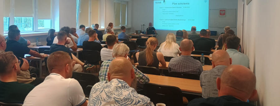 Na zdjęciu sala szkoleniowa – uczestnicy siedzą przy stołach, słuchają prelegenta, na ekranie widoczny jest slajd z planem szkolenia dotyczącym Elektronicznego Dziennika Budowy i Cyfrowej Książki Obiektu Budowlanego.