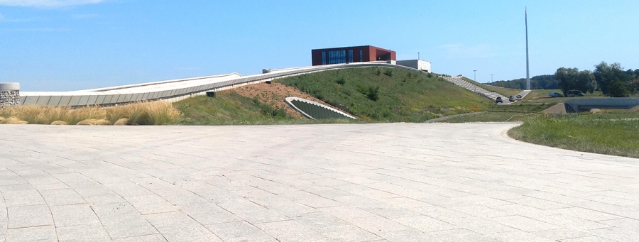 Na zdjęciu widać budynek muzeum na wzgórzu. W oddali widoczny amfiteatr do oglądania rekonstrukcji historycznych oraz maszt. 