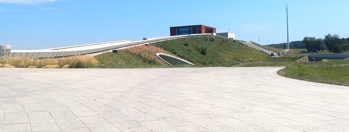 Na zdjęciu widać budynek muzeum na wzgórzu. W oddali widoczny amfiteatr do oglądania rekonstrukcji historycznych oraz maszt. 