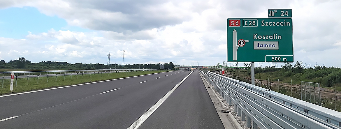 Na zdjęciu widać pustą trasę z dwoma pasami w każdym kierunku. Na pierwszym planie po prawej stronie stoi zielona tablica informująca o przebiegu trasy: w prawo - skręt na Koszalin, prosto – droga na Szczecin.